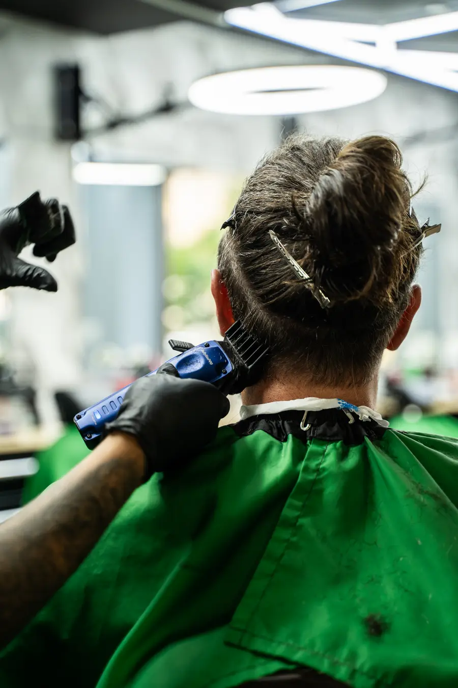 Clipper work on an undercut, hair clipped up, green cape, from behind